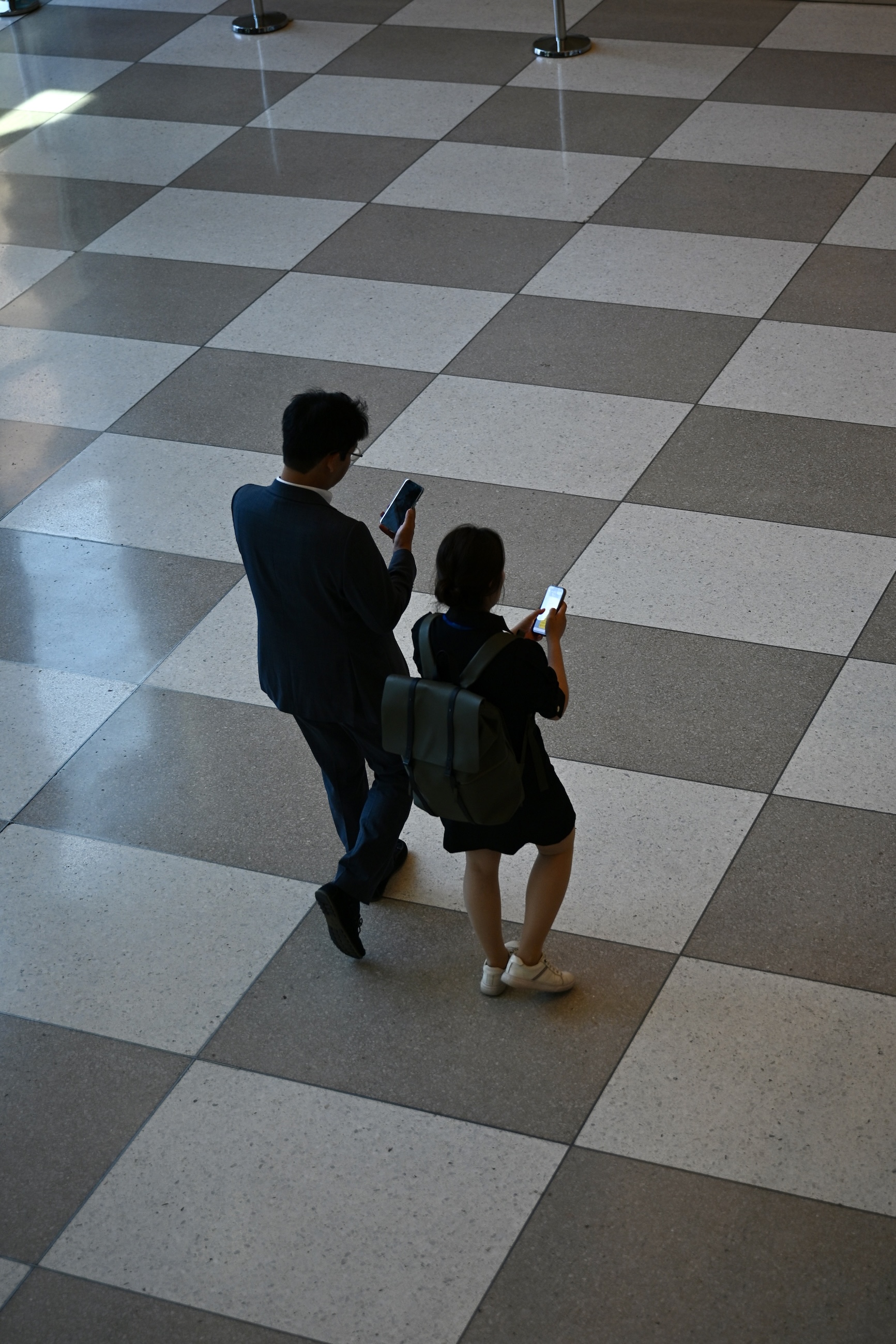 Two people checking their phones while crossing a tiled United Nations lobby